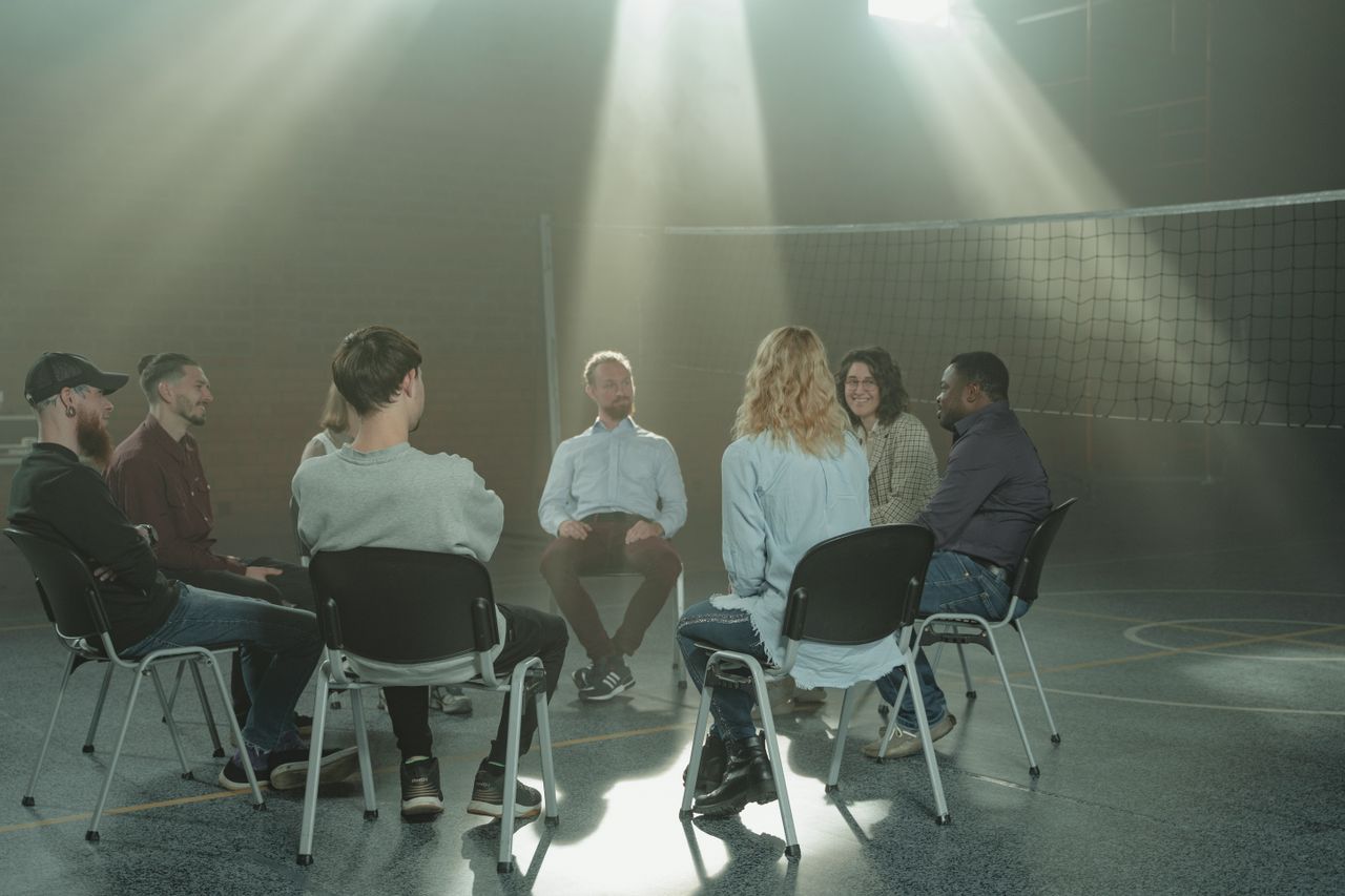 services-01 A small group engaging in a therapy session indoors, under rays of sunlight.