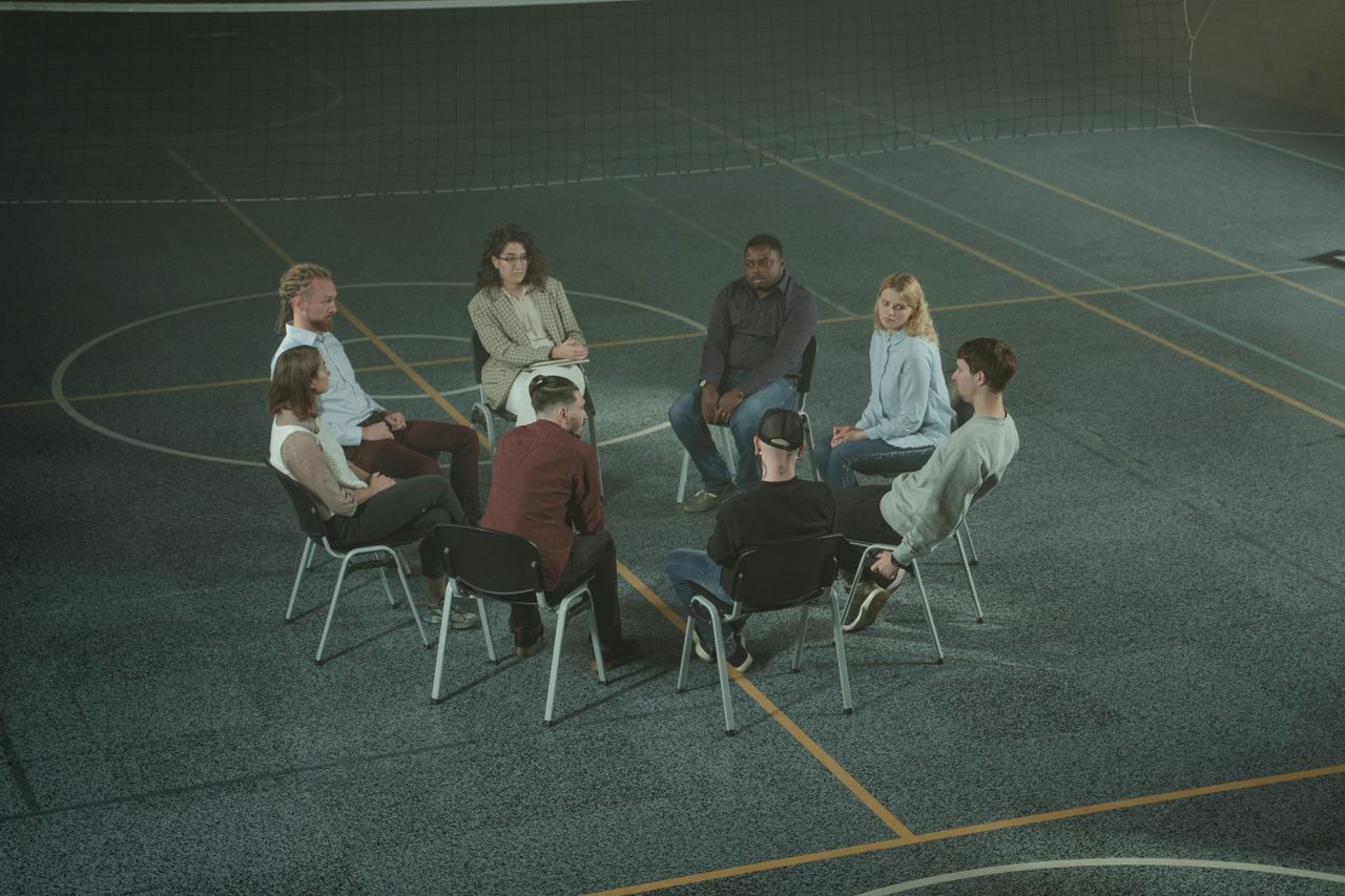 services-01 A diverse group of people sitting in a circle during a therapy session in a sports hall.